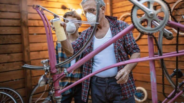 man spray painting a bike frame while boy watches