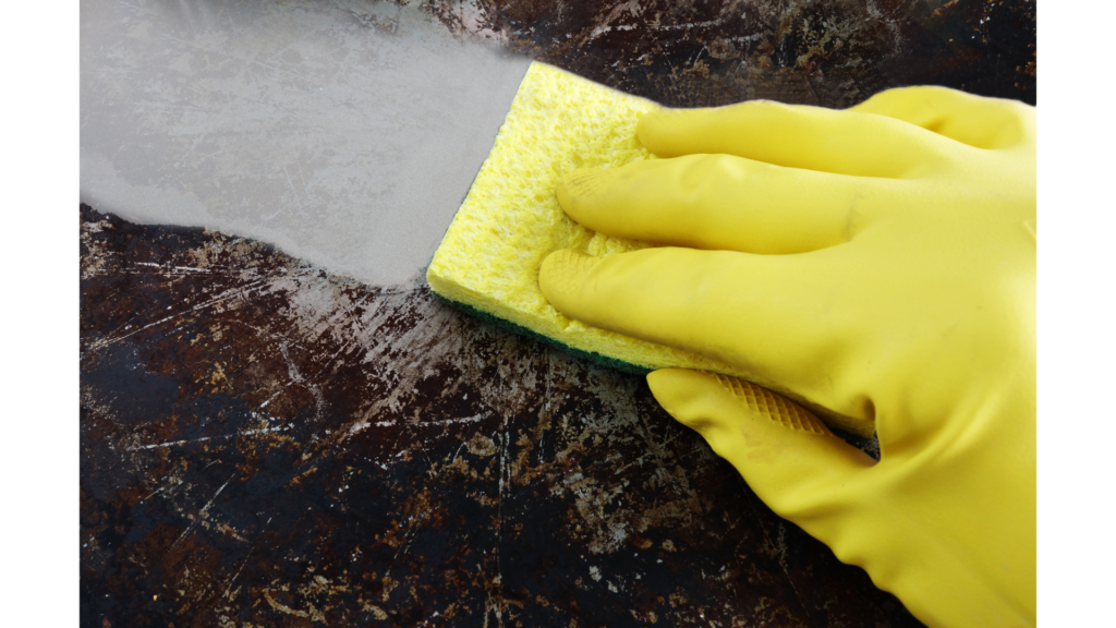 Close up of someone wearing rubber gloves scrubbing the bottom of a burnt pan - learn how to degrease a pan quickly!