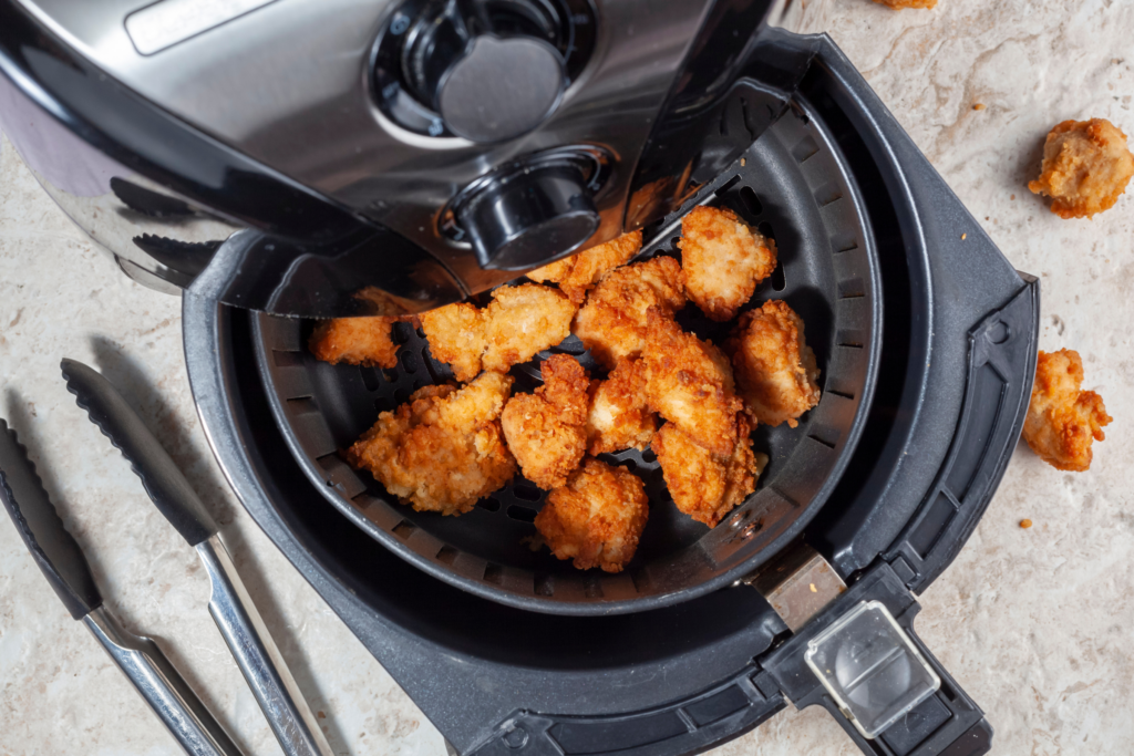 Breaded chicken bites inside and air fryer, next to a pair of rubber tongs.