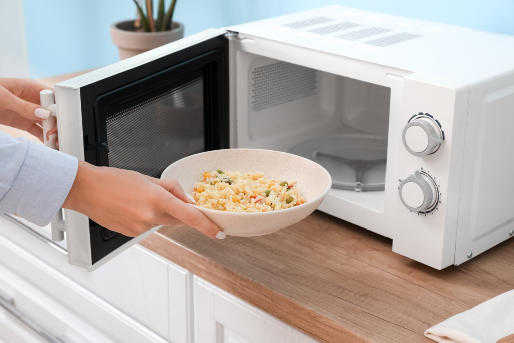 A person holds a bowl of food in front of an open microwave.