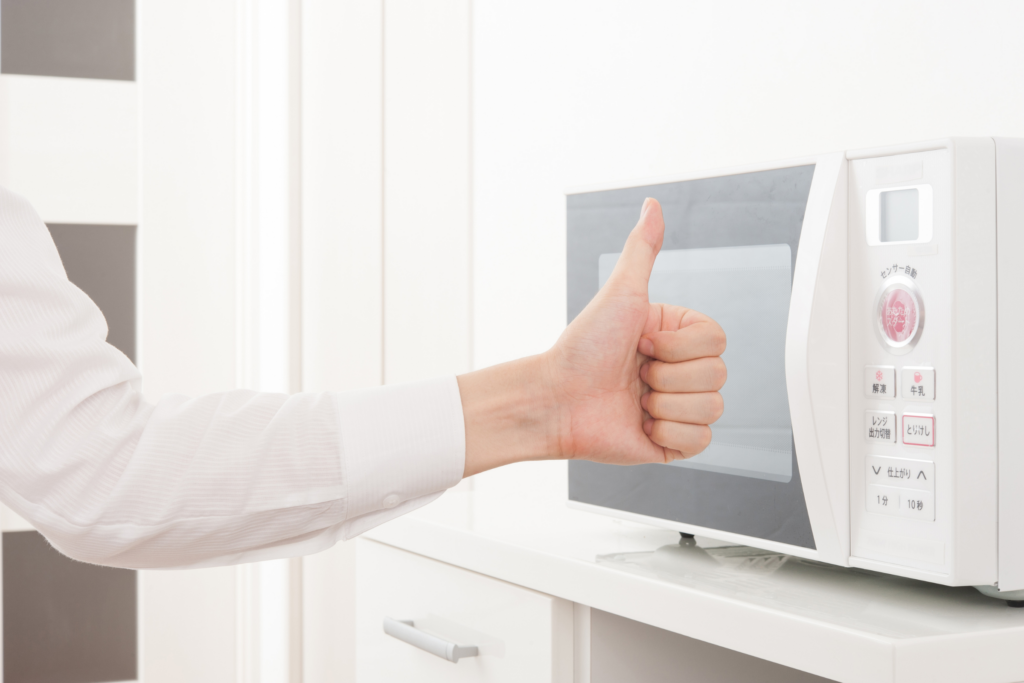 A person holds their thumb up in front of a microwave.