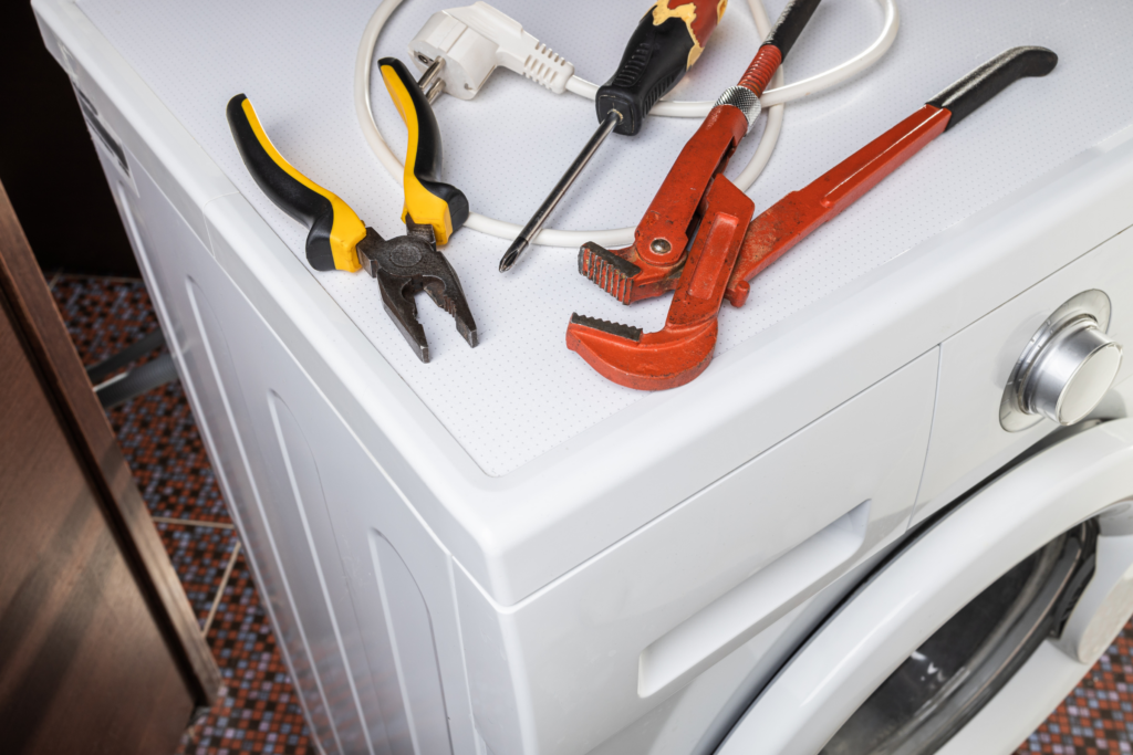 A pair of plyers, a wrench, and a screw driver sit on top of a washing machine.
