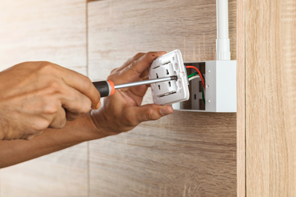 Wiring is exposed as a person replaces a wall outlet using a screwdriver.