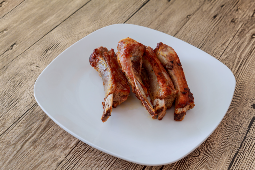Perfectly cooked ribs served on a white plate on top of a wooden table or bench.