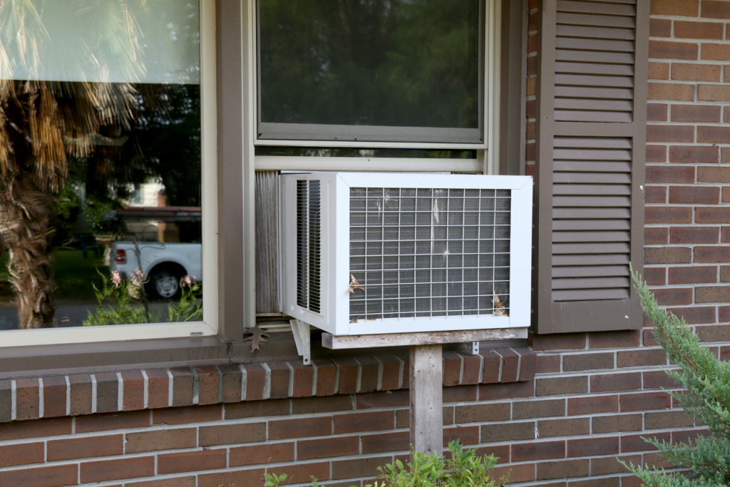 A white window air conditioner viewed from the outside of a brick building. 